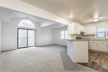 A spacious, empty room with a kitchenette and a large window with a view of a balcony